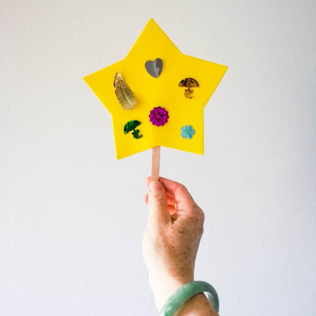 A hand holding a handmade yellow star decorated with tiny treasures