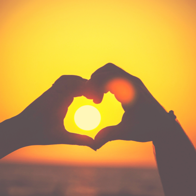 Hands forming a heart around the setting sun