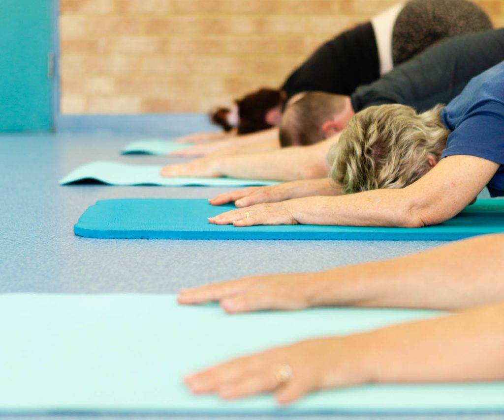 Class members resting in child’s pose on turquoise yoga mats
