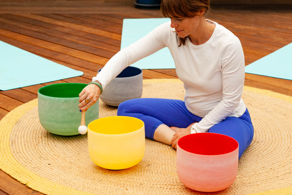 Heather playing a yellow singing bowl surrounded by colourful bowls