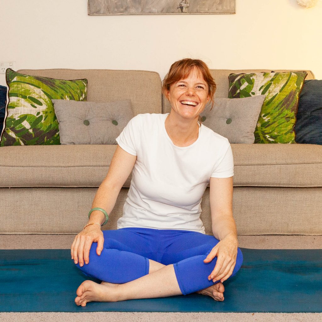 Heather smiling while seated on a yoga mat in her home clinic