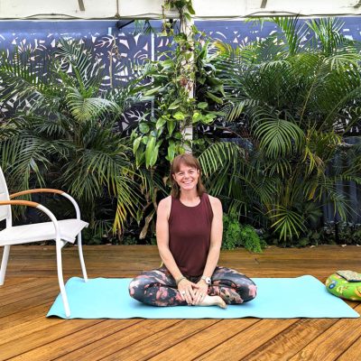 Heather seated comfortably on a yoga mat in a leafy garden